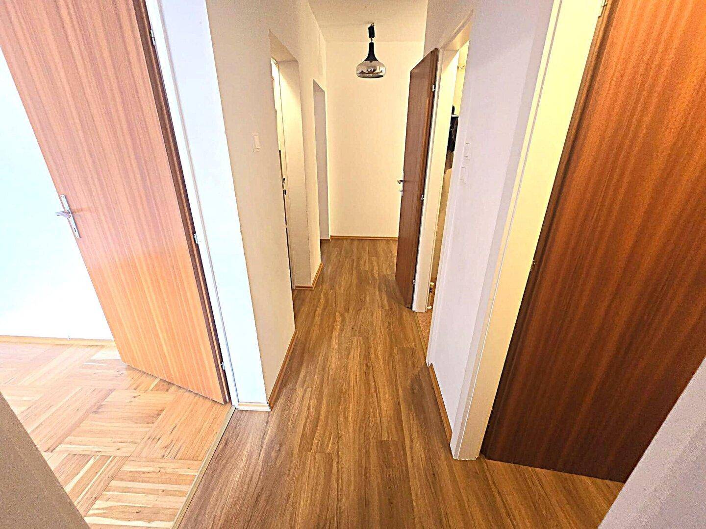 Langer Flur mit Holzlaminatboden und mehreren Türen, die zu den angrenzenden Räumen führen.