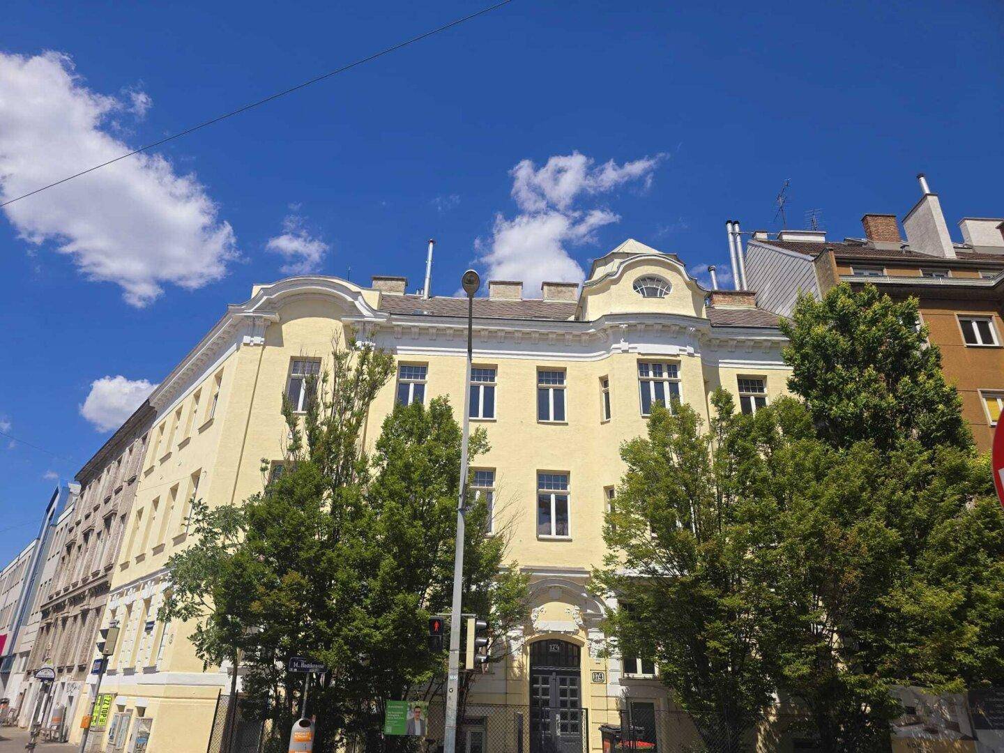Elegantes Altbaugebäude mit gelber Fassade, charakteristischer Architektur und hohen Fenstern unter blauem Himmel.