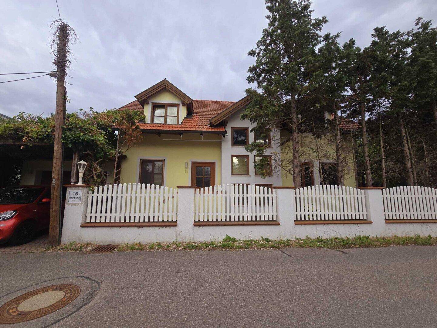 Vorderansicht des Hauses von der Straße mit weißem Zaun und Carport.
