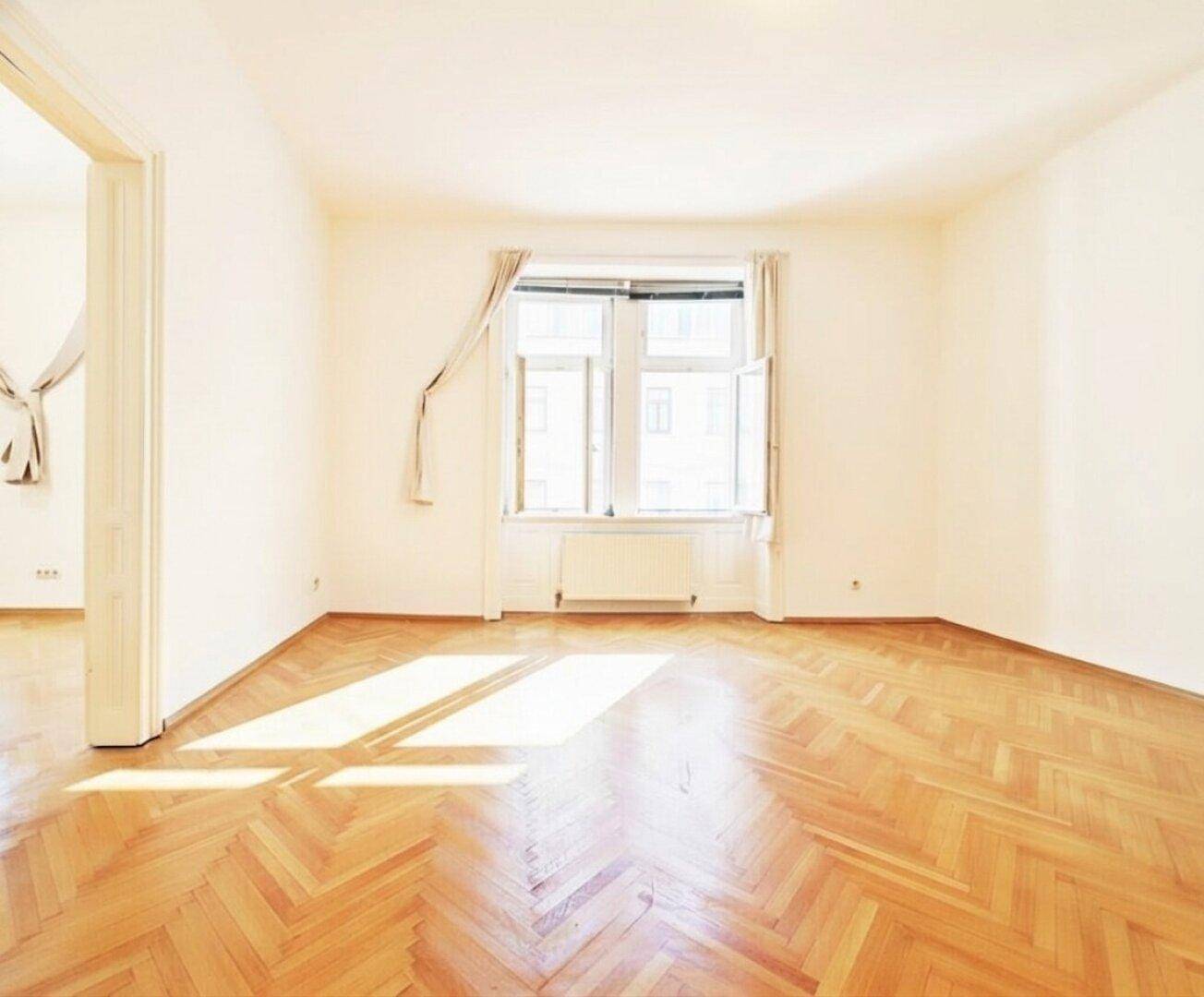 Freundliches Zimmer mit Fischgrätparkett und einem großen Fenster, das für eine angenehme Helligkeit sorgt.