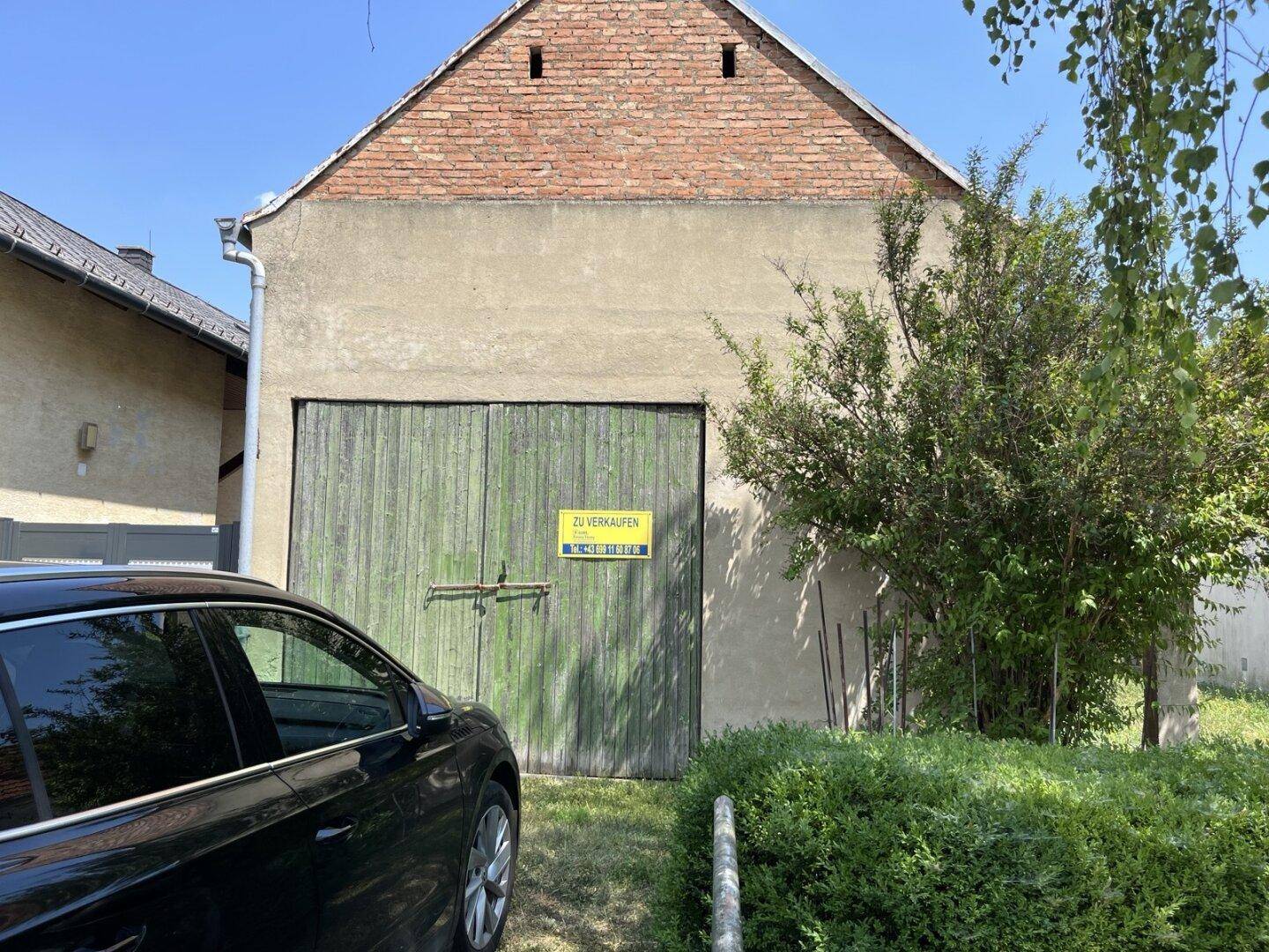 Fassade eines alten Scheunengebäudes mit Holztoren und einem "Zu Verkaufen"-Schild.