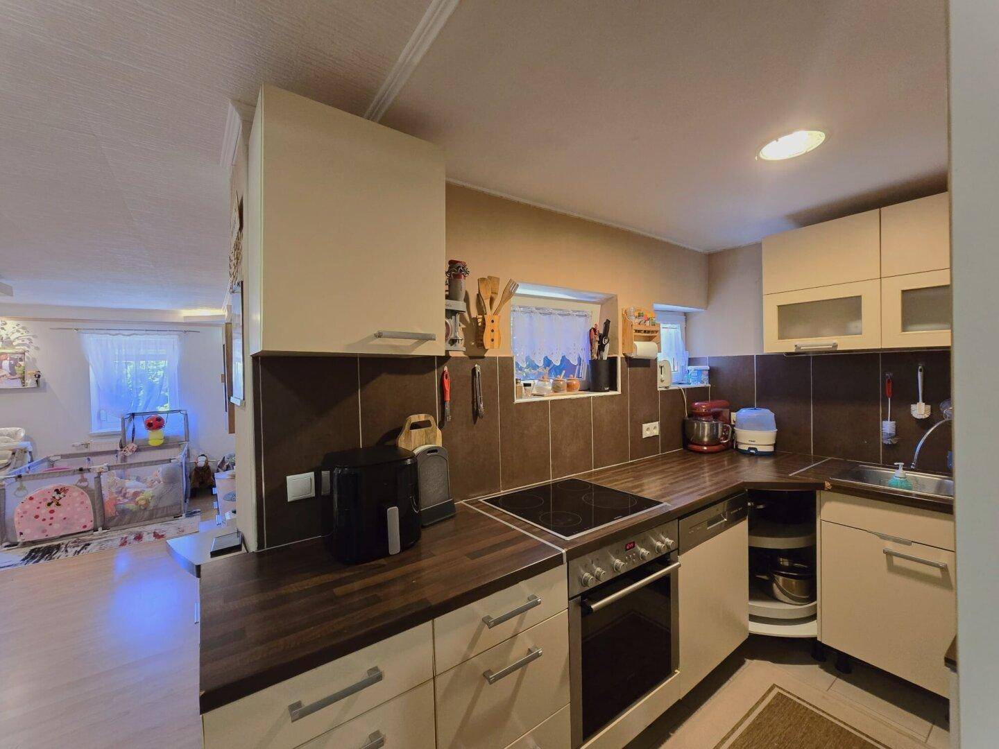 Funktionale Küche mit beigen Schränken, dunklen Arbeitsplatten und Fliesenrückwand.