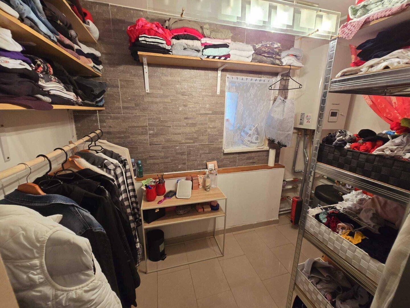Funktionaler Abstellraum mit Regalen, Kleiderstangen und Fliesenboden.