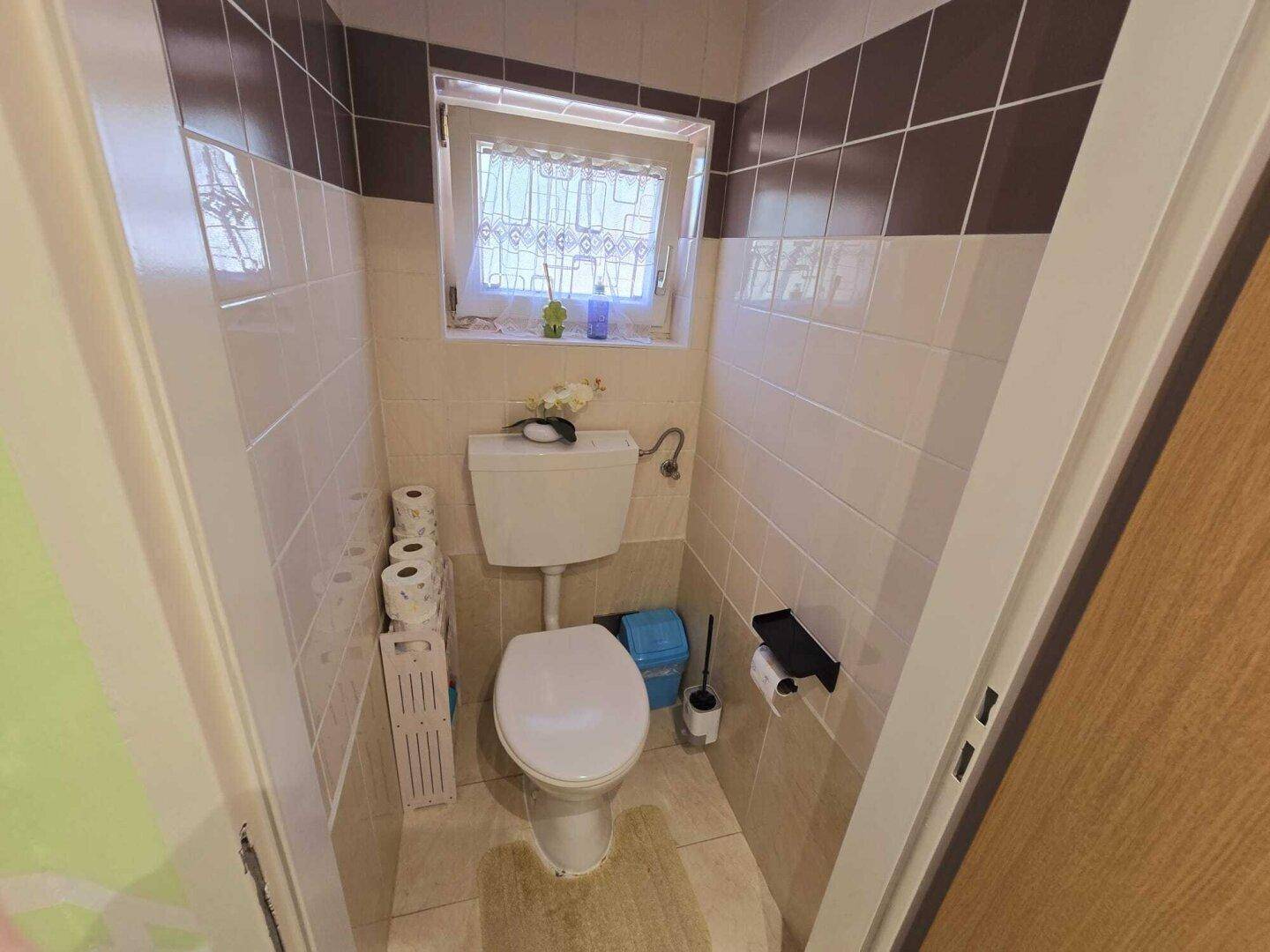 Kleines WC mit Fliesenwänden, Toilette und Fenster.