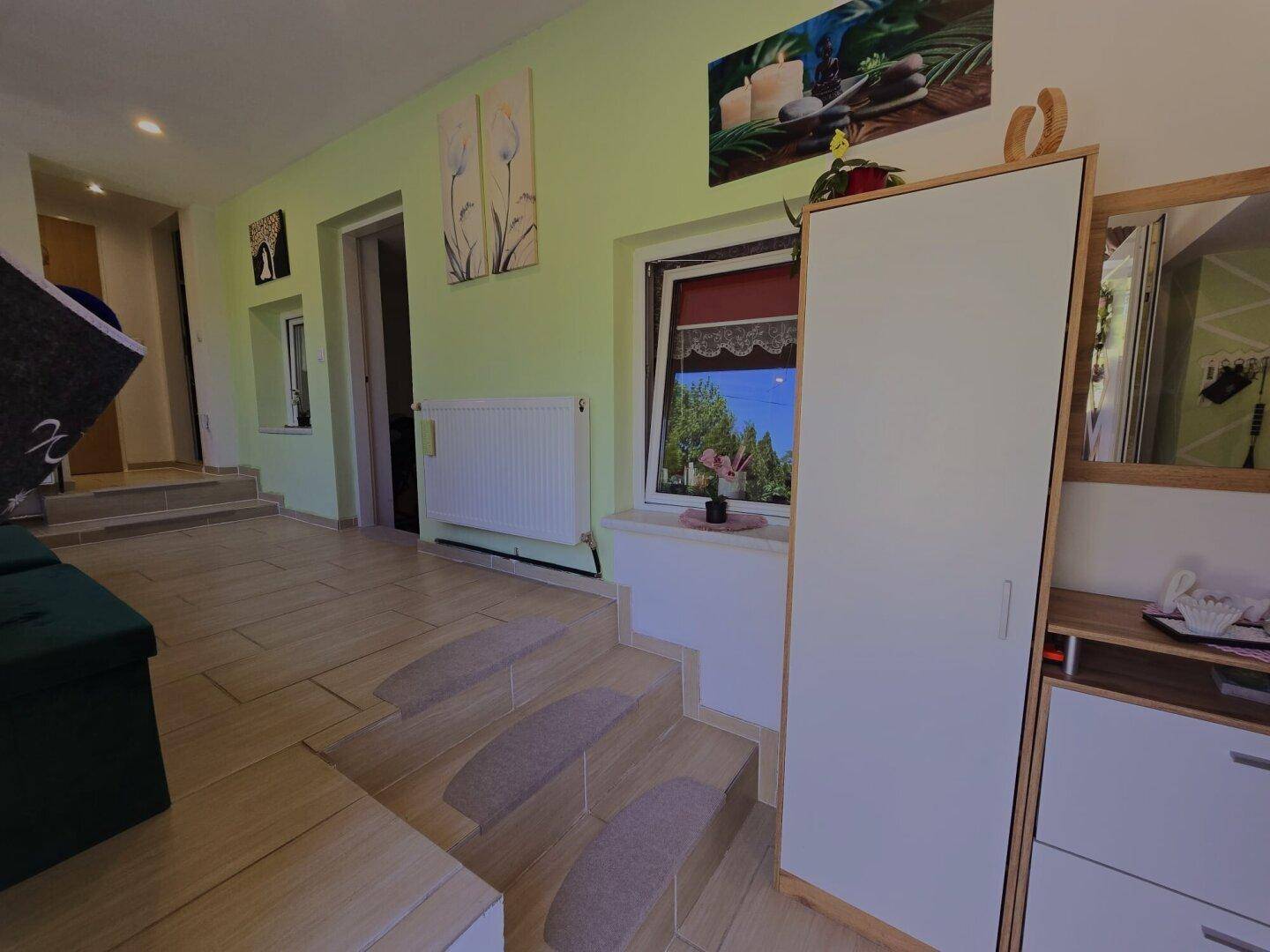 Heller Flur mit Stufen, Fliesenboden und grünen Wänden, geschmückt mit Kunstwerken.