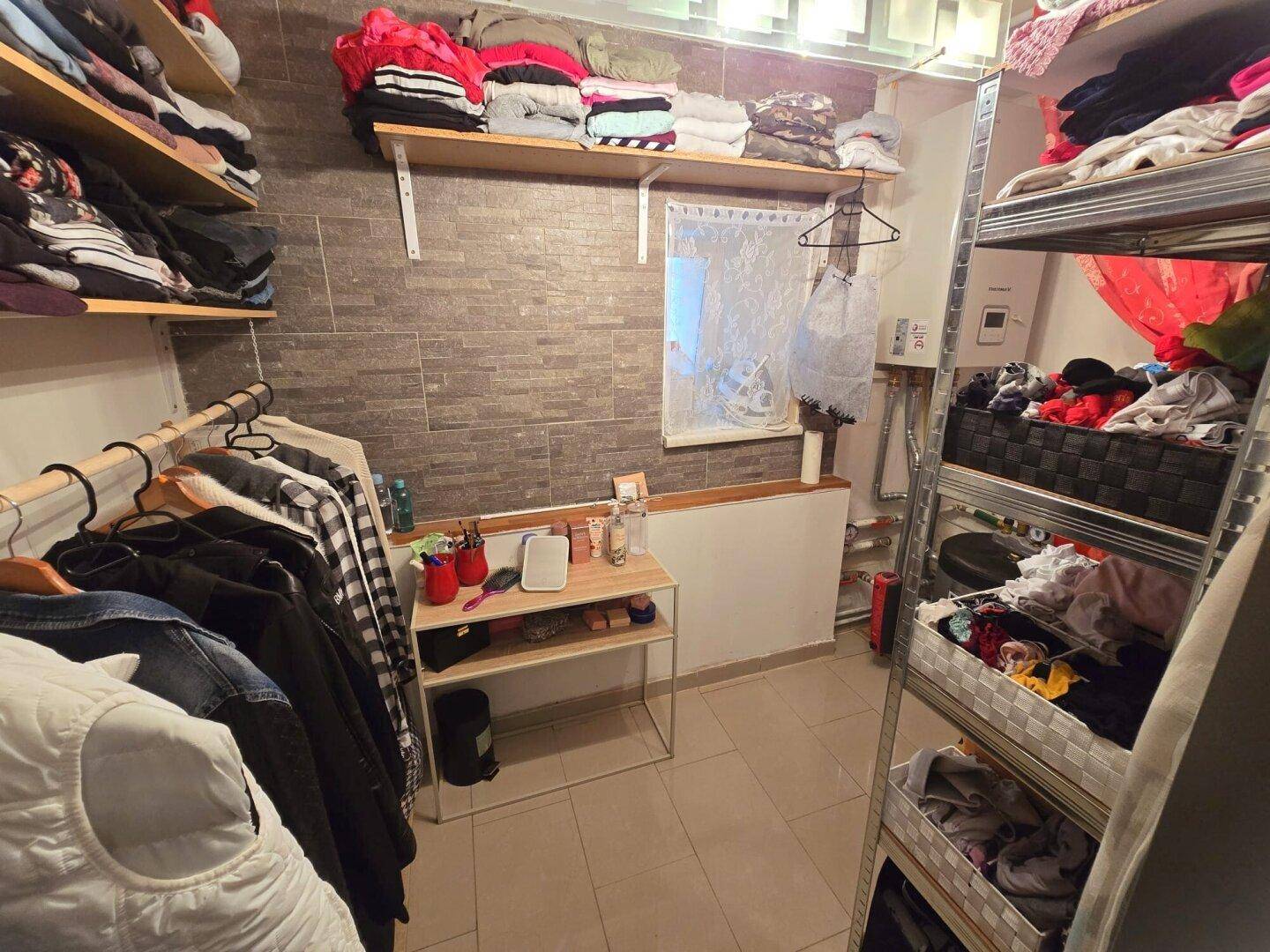 Funktionaler Abstellraum mit Regalen, Kleiderstangen und Fliesenboden.