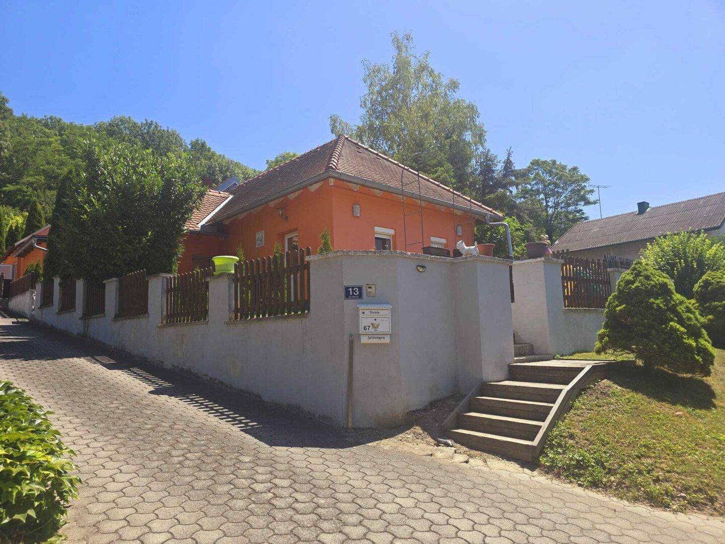 Hausansicht mit oranger Fassade, gepflasterter Auffahrt und Treppenzugang.