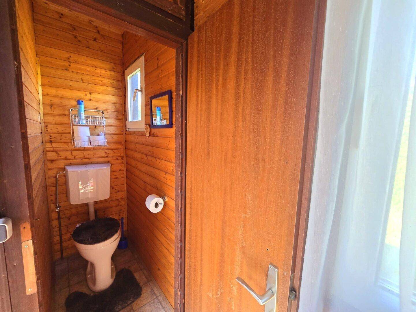 Kleines WC mit holzvertäfelten Wänden und einem Fenster für natürliches Licht.