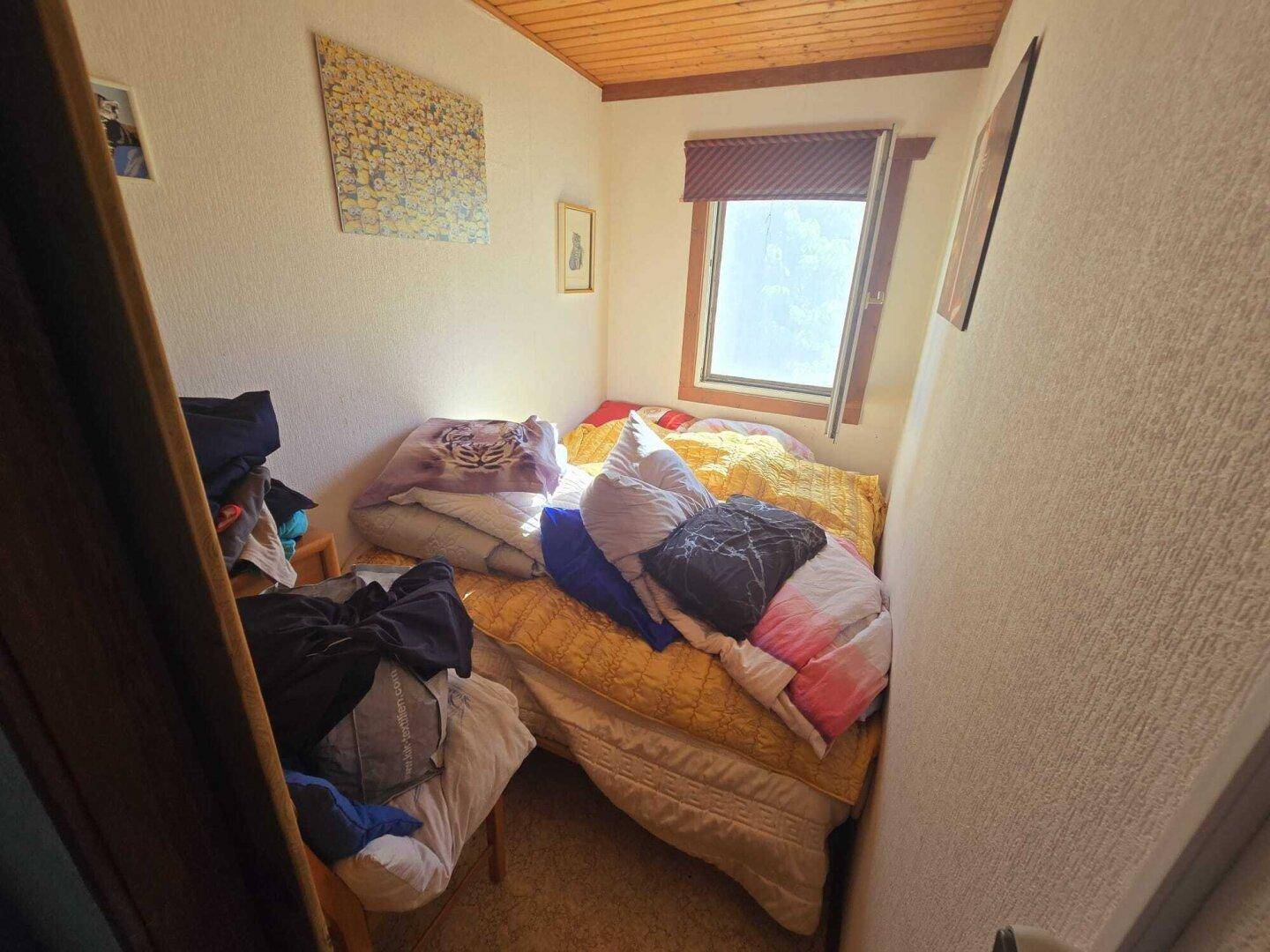 Kleines Schlafzimmer mit einem Bett, einem Fenster und einer Holzdecke.