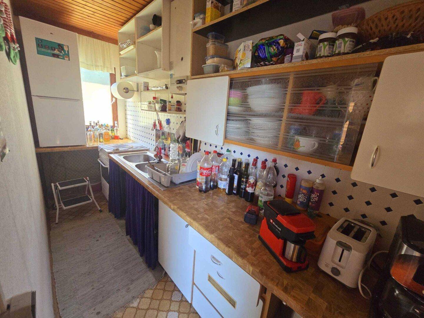 Kleine, funktionale Küche mit Holztheke, weißen Schränken und einem Kühlschrank.