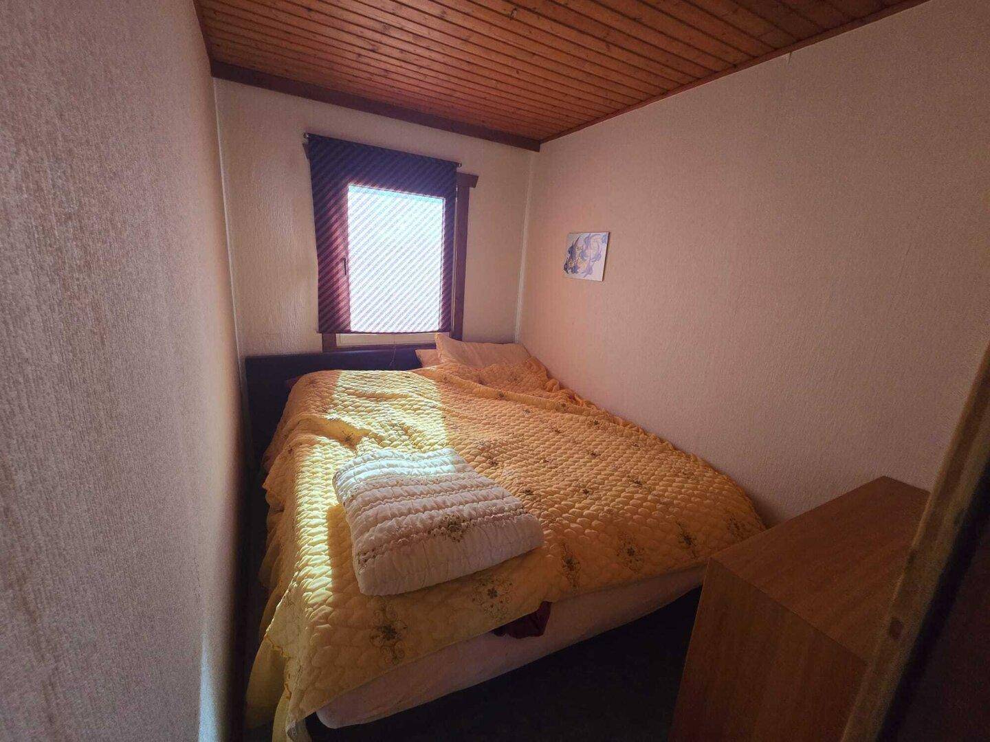 Gemütliches Schlafzimmer mit einem Bett, einem Fenster und einer Holzdecke.