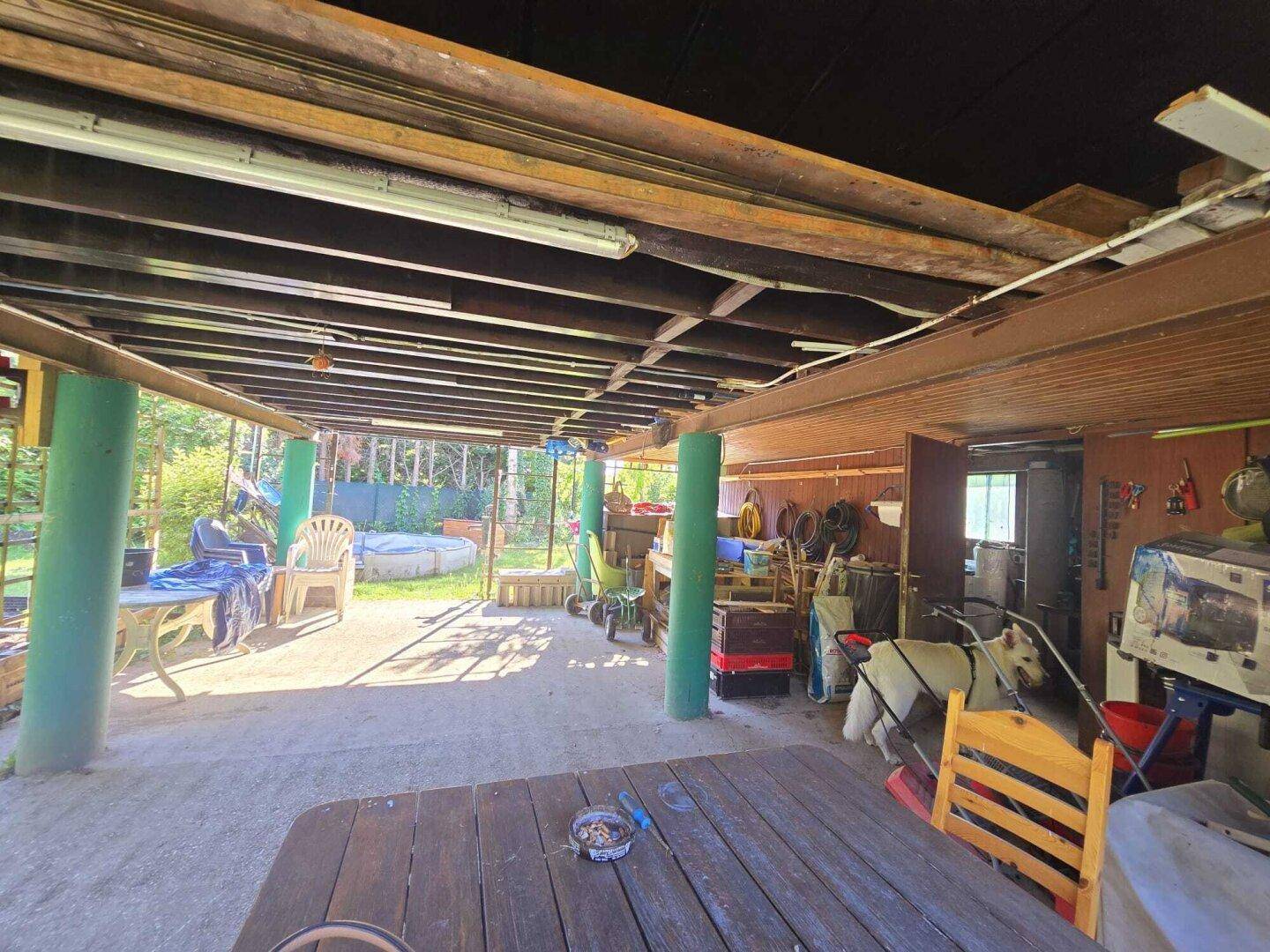 Überdachter Außenbereich unter dem Haus mit Holzbalken und einem Holztisch.