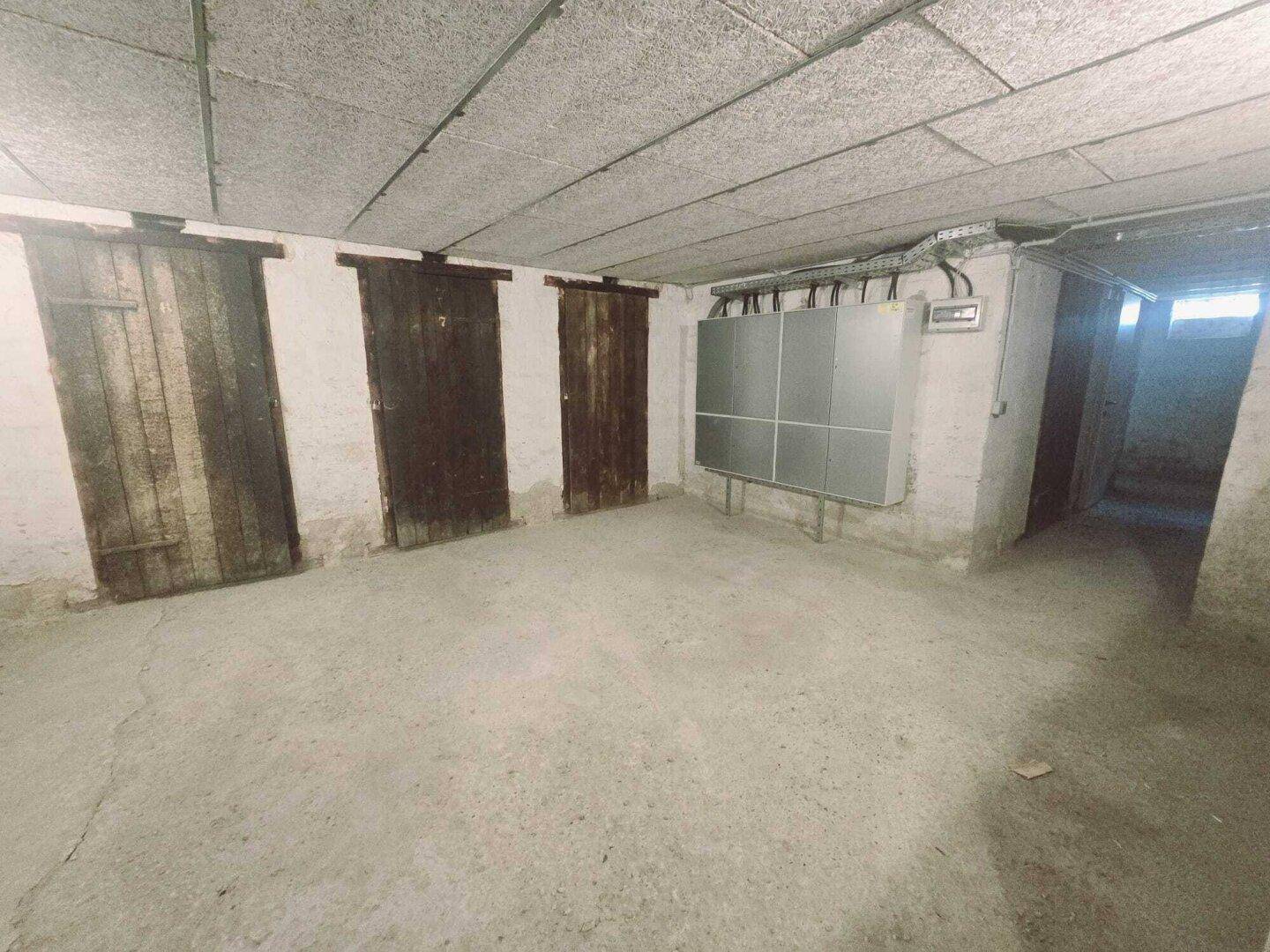 Unausgebauter Kellerraum mit Betonboden und mehreren Holztüren zu Abteilen.