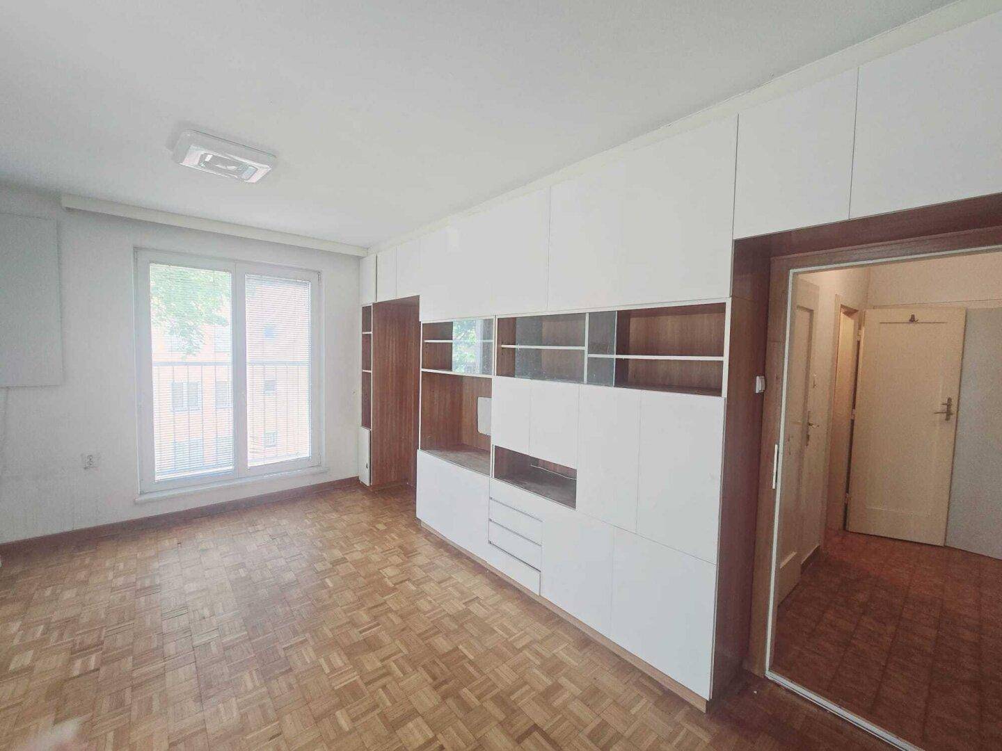 Helles Wohnzimmer mit Parkettboden und modernen Einbauschränken, mit Balkonzugang.