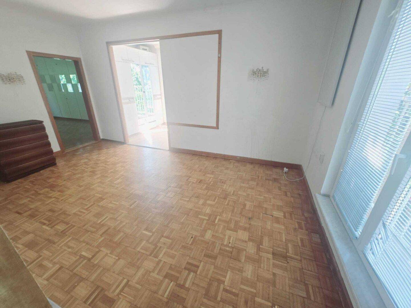 Wohnzimmer mit Parkettboden und einer breiten Öffnung zu einem angrenzenden Raum.