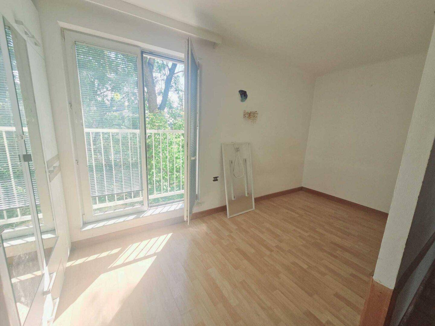 Helles Schlafzimmer mit Holzboden und Zugang zu einem französischen Balkon mit Blick ins Grüne.