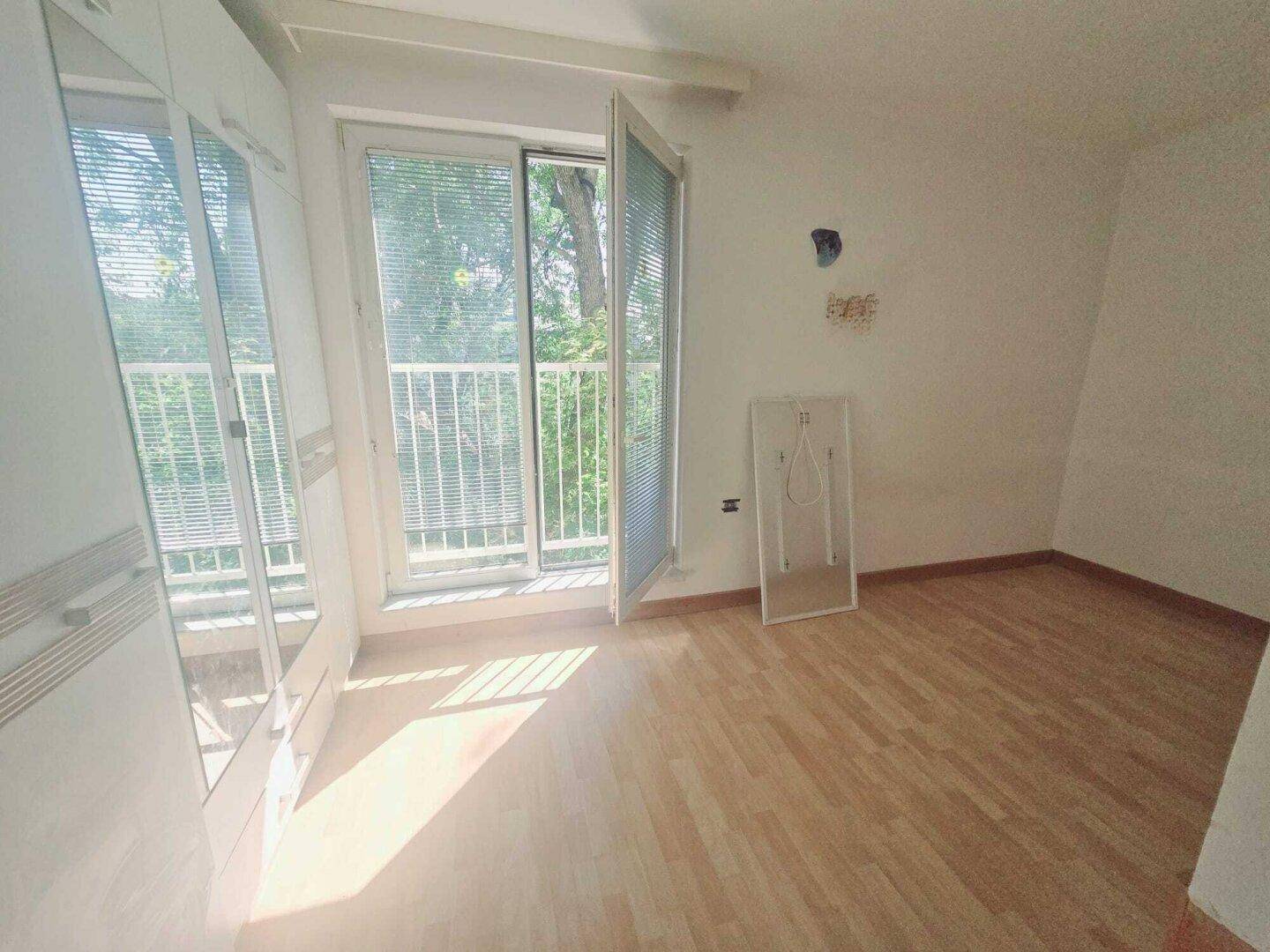 Schlafzimmer mit Holzboden, Einbauschrank und Zugang zu einem französischen Balkon.