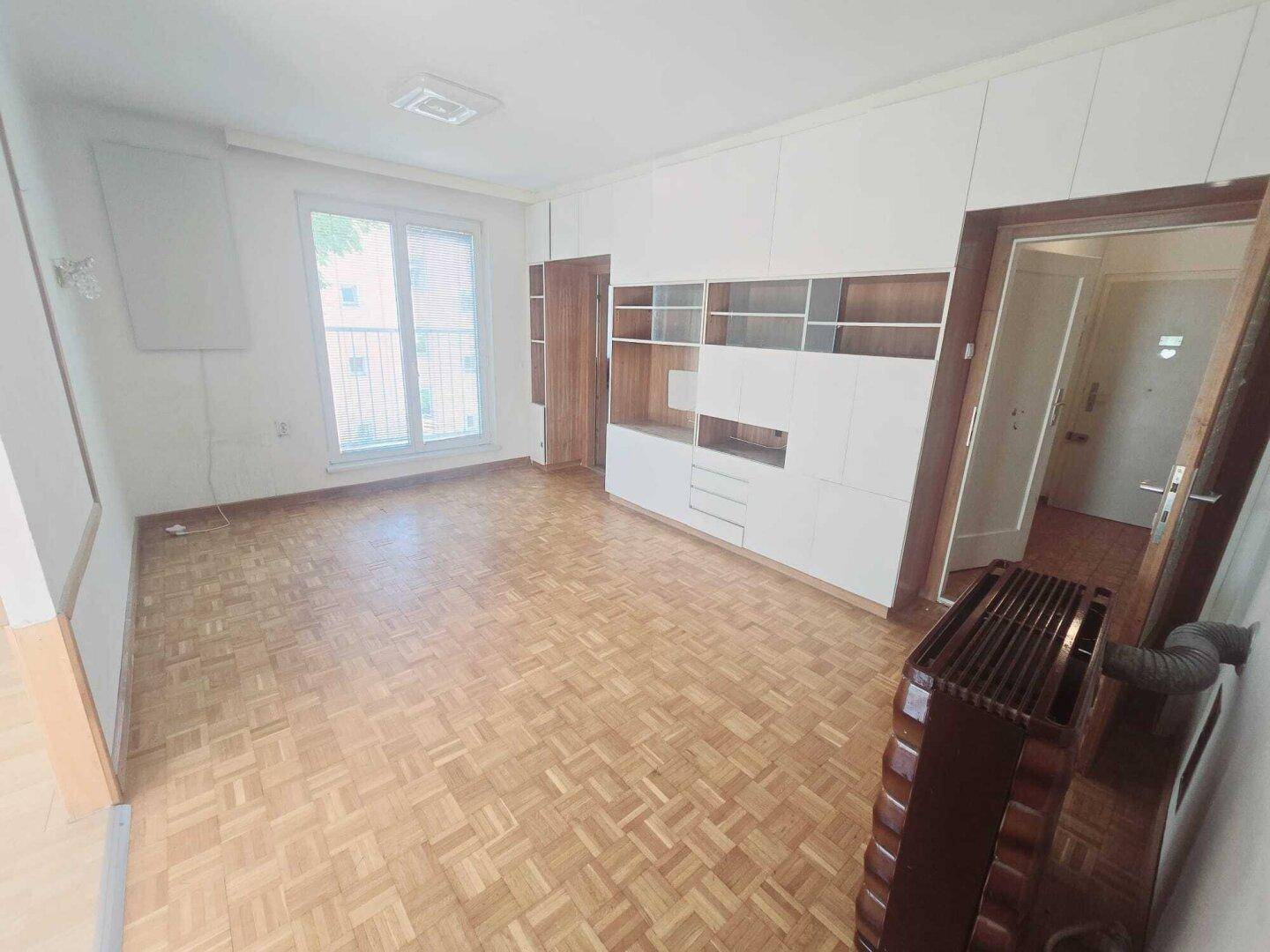 Geräumiges Wohnzimmer mit Parkettboden, Einbauschränken und einem Heizkörper am Fenster.