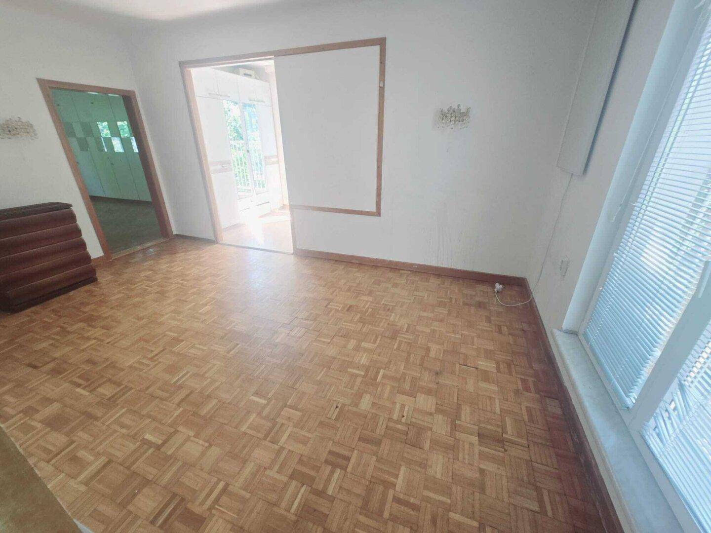Wohnzimmer mit Parkettboden und einer breiten Öffnung zu einem angrenzenden Raum.