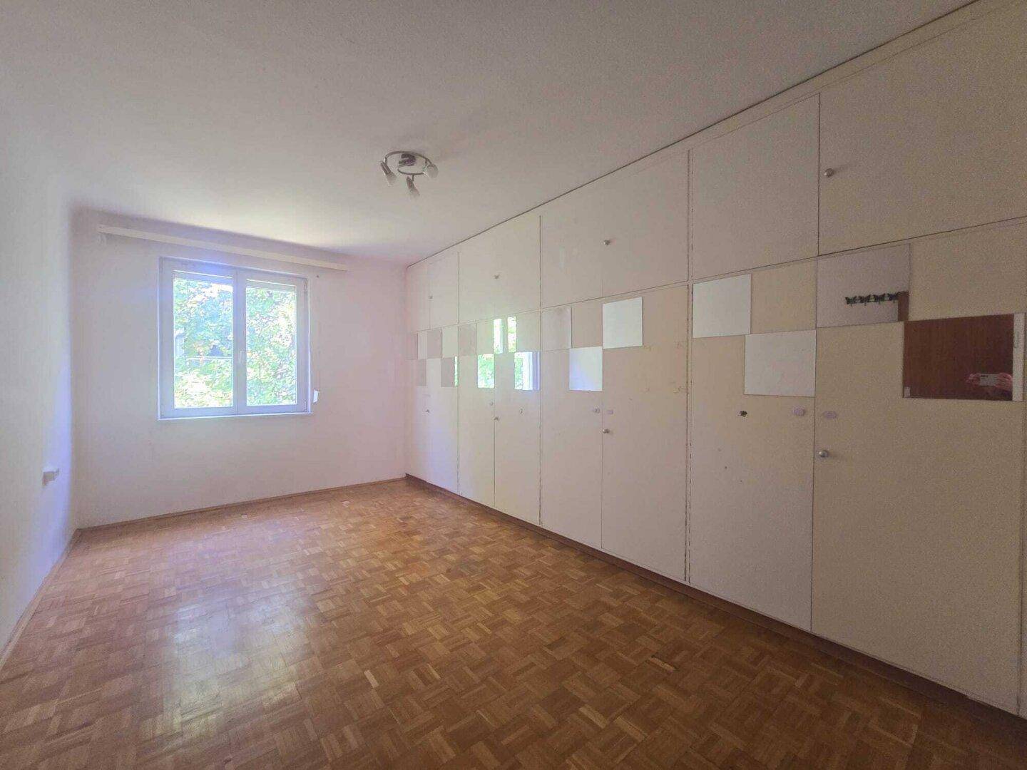 Schlafzimmer mit Parkettboden und einer Wand voller integrierter Einbauschränke.
