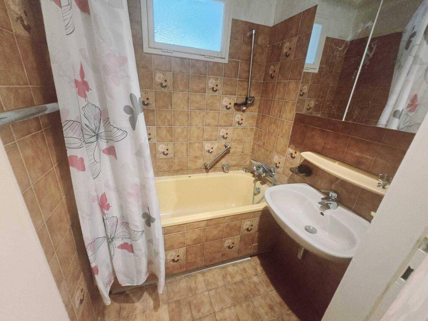 Badezimmer im 80er-Jahre-Stil mit Badewanne, Waschbecken und braunen Fliesen.