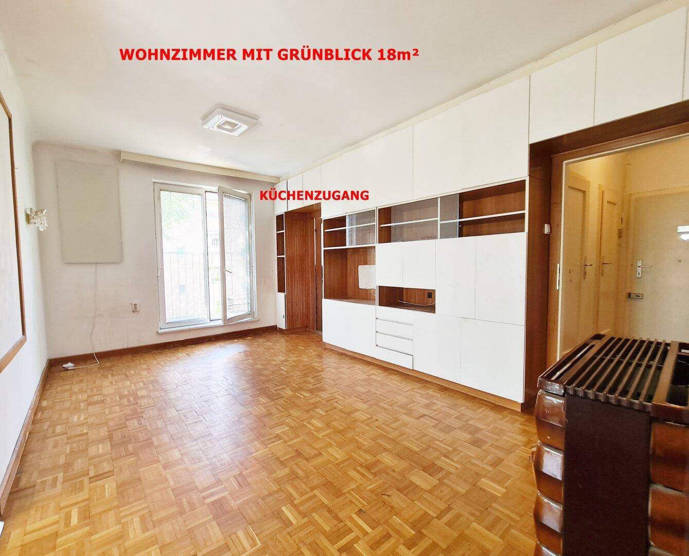 Geräumiges Wohnzimmer mit Parkettboden, Einbauschränken und Zugang zur Küche sowie einem Balkon mit Grünblick.