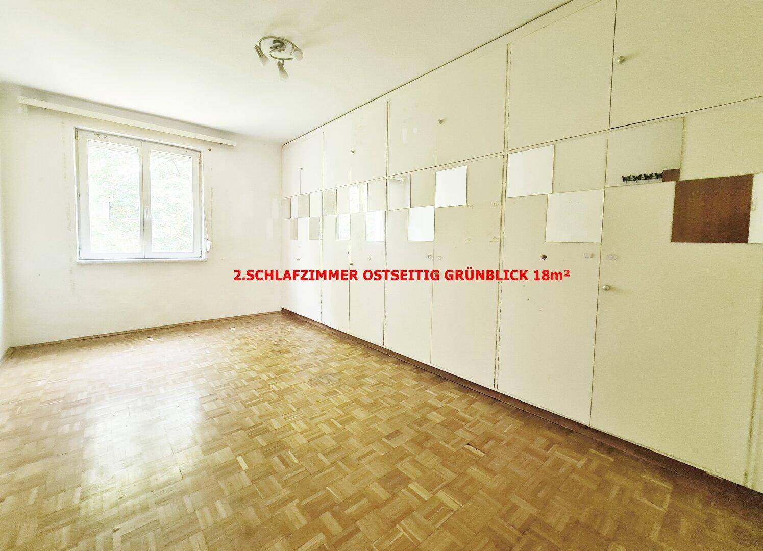 Zweites Schlafzimmer mit Parkettboden, integrierten Schränken und Fenster mit Ostausrichtung und Grünblick.