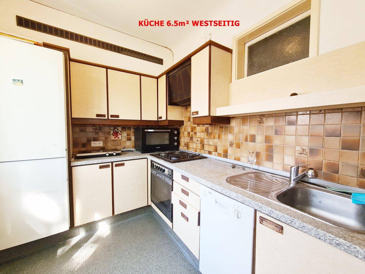 Funktionale Küche mit beigen Schränken, Fliesenrückwand und integrierten Geräten wie Geschirrspüler und Backofen.