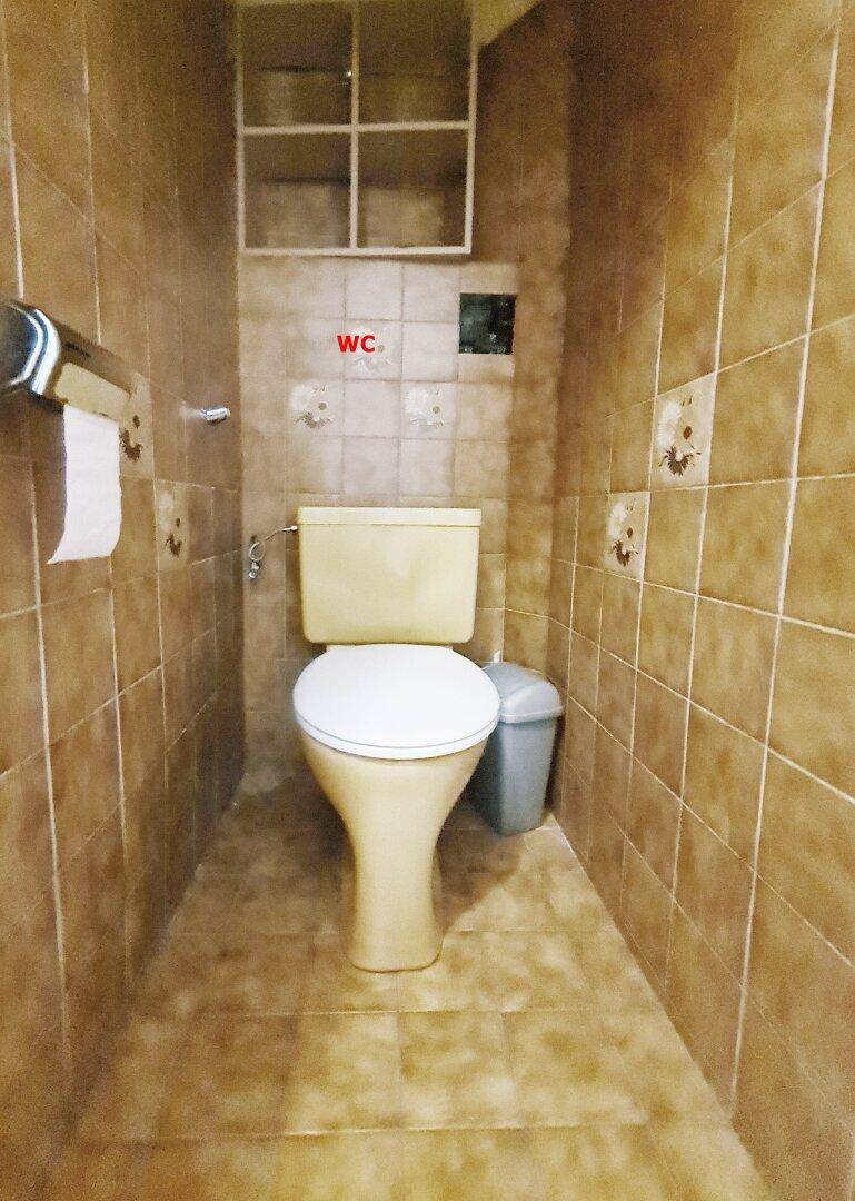 Separates WC mit braunen Fliesen an Wänden und Boden sowie einer beige-farbenen Toilette.