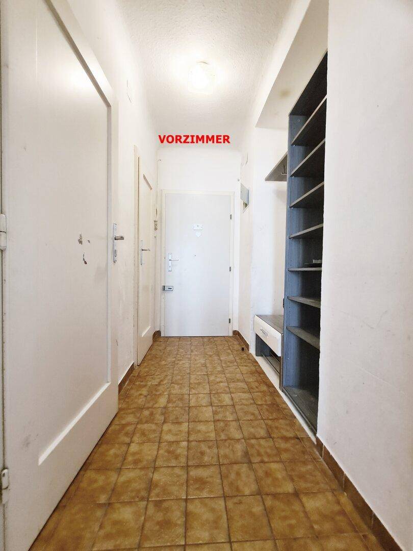 Eingangsbereich mit Fliesenboden, weißen Wänden und einem praktischen offenen Regal für Stauraum.