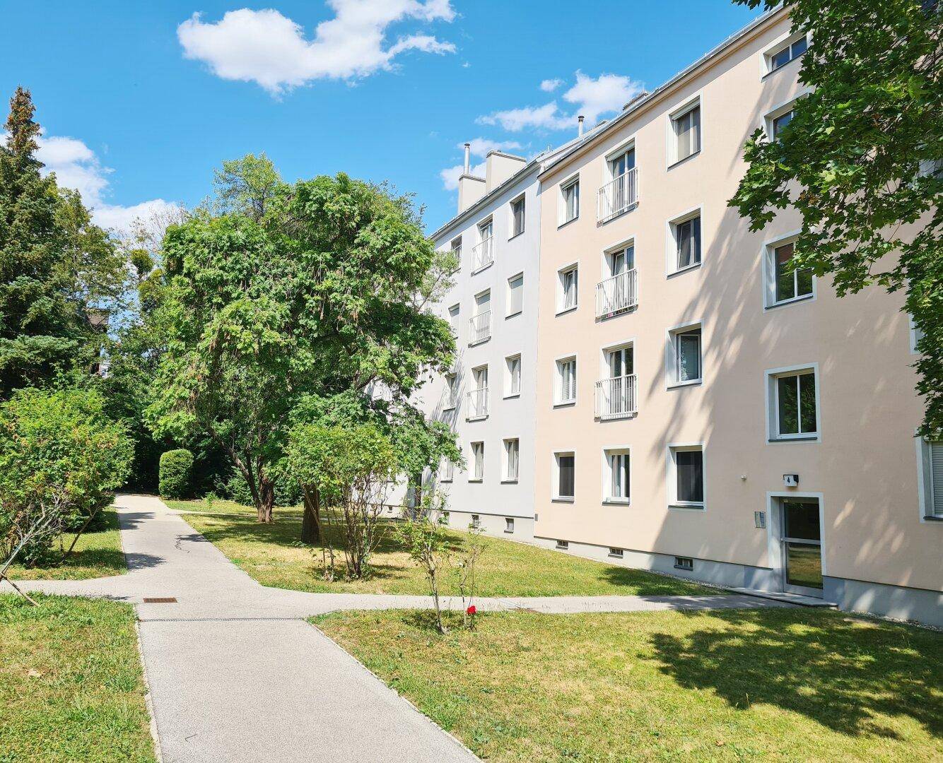 Wohngebäude mit mehreren Balkonen, umgeben von gepflegten Grünflächen und Bäumen.
