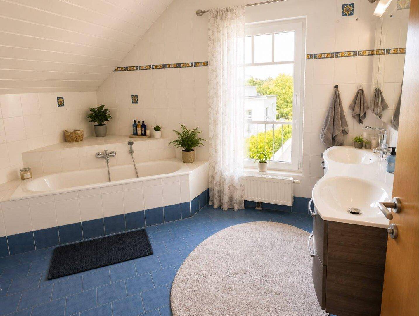 Geräumiges Badezimmer mit Badewanne, Doppelwaschbecken und Fenster unter der Dachschräge.