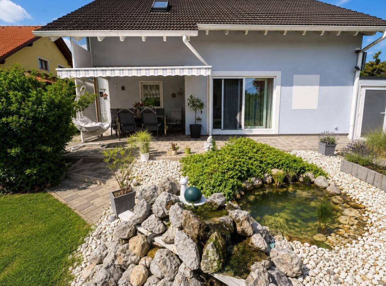 Hinterhof mit Steingarten, Teich und überdachter Terrasse, ideal für entspannte Stunden im Freien.