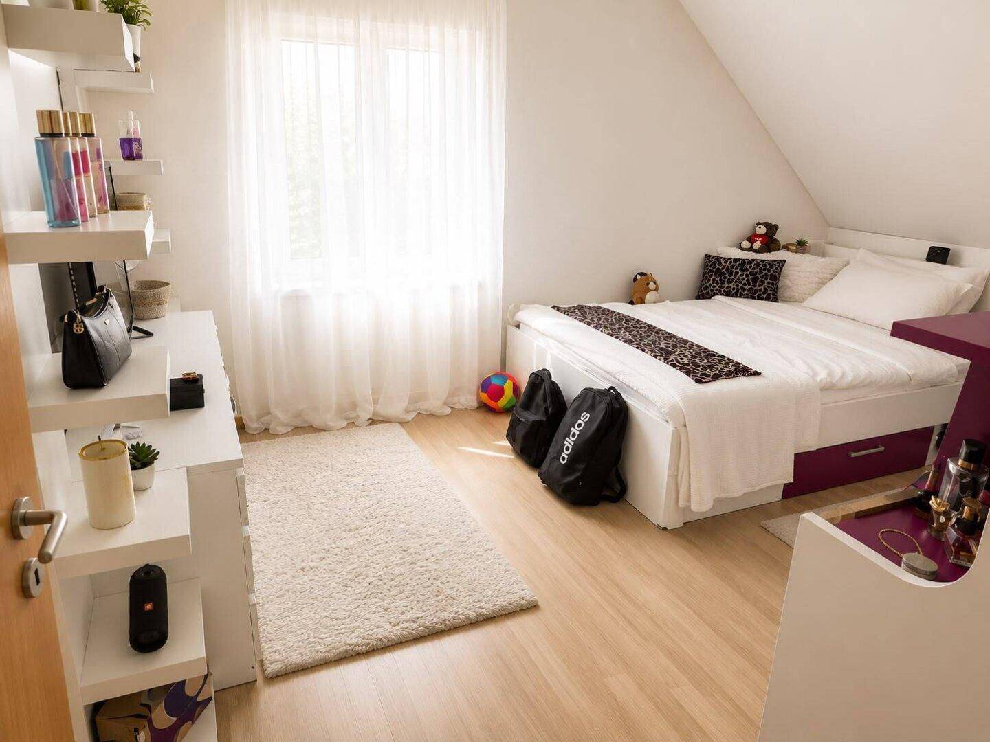 Gemütliches Schlafzimmer mit Dachschräge, hellem Laminatboden und großem Fenster.