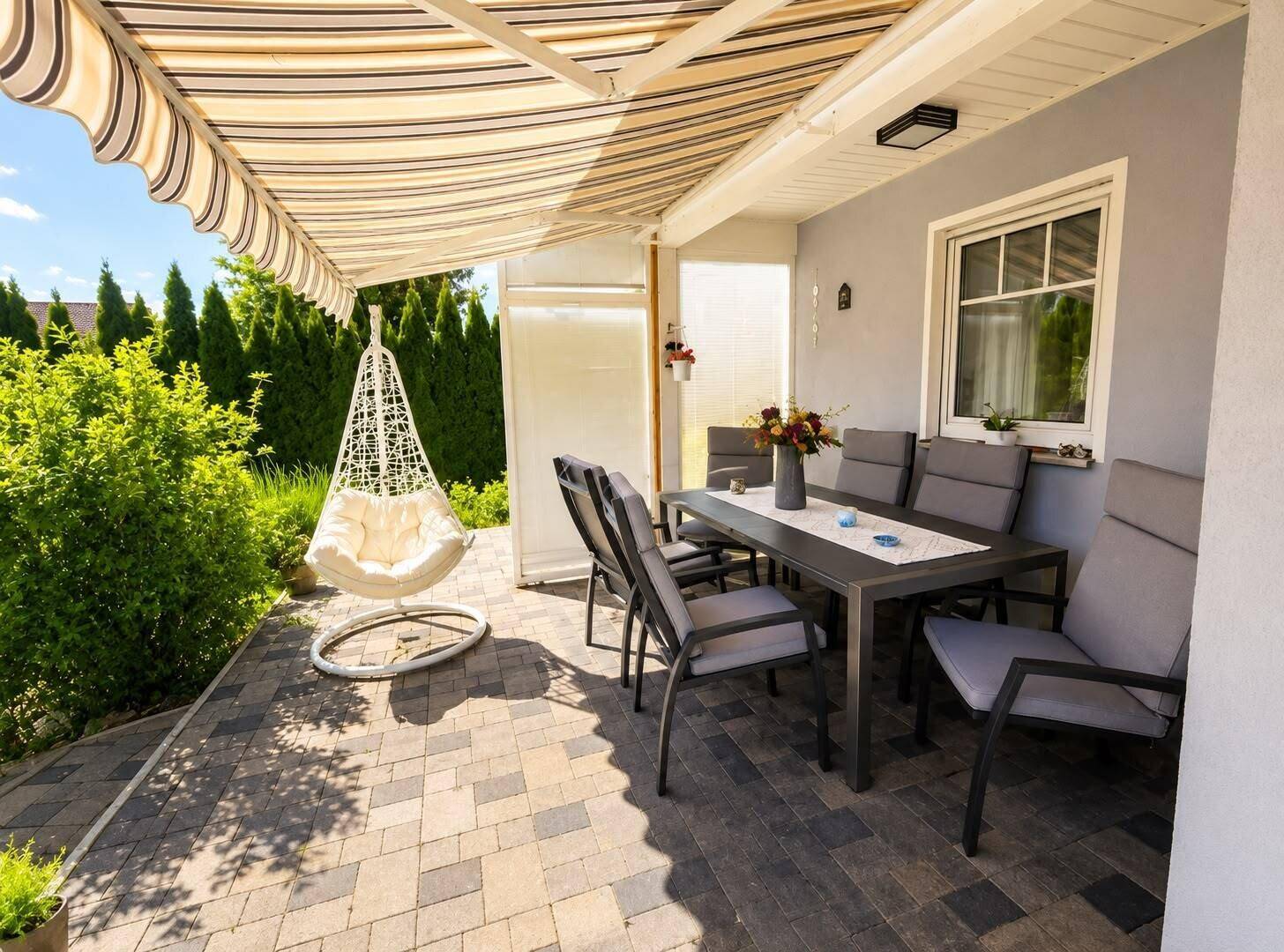 Überdachte Terrasse mit Esstisch und Hängesessel, ideal für Mahlzeiten im Freien.