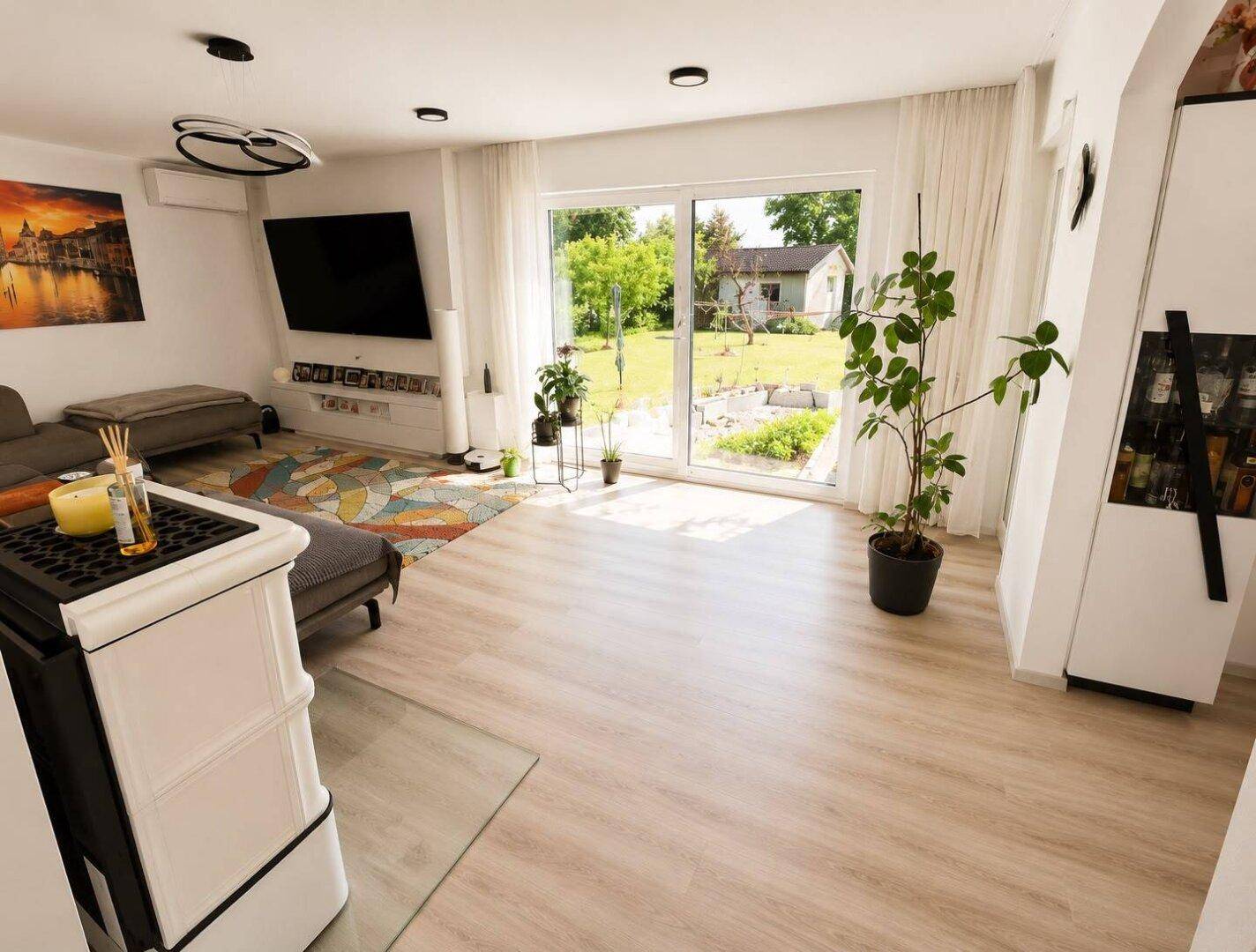 Modernes Wohnzimmer mit großzügiger Fensterfront, Kaminofen und Zugang zum Garten.