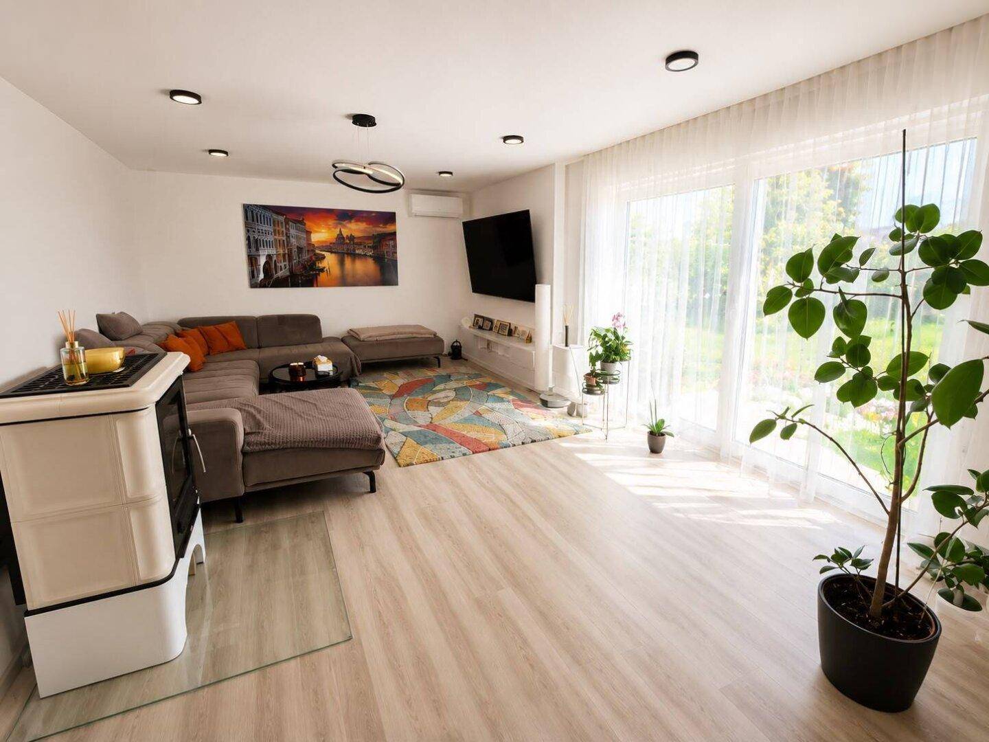 Heller Wohnbereich mit bequemer Couch, Kaminofen und großen Fenstern zum Garten.