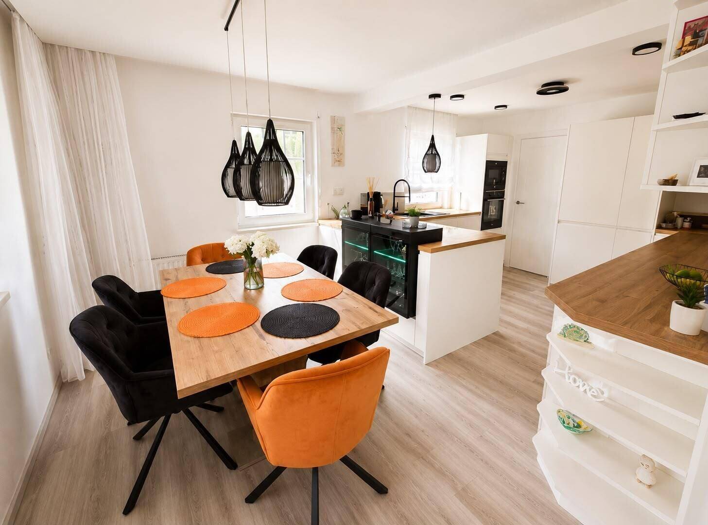 Heller Essbereich mit modernem Holztisch und farbigen Stühlen, offen zur Küche.