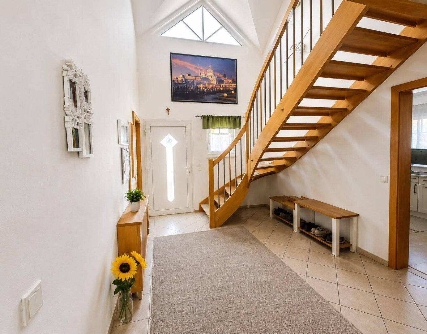 Geräumiger Flur mit offener Holztreppe, hohen Decken und viel natürlichem Licht.