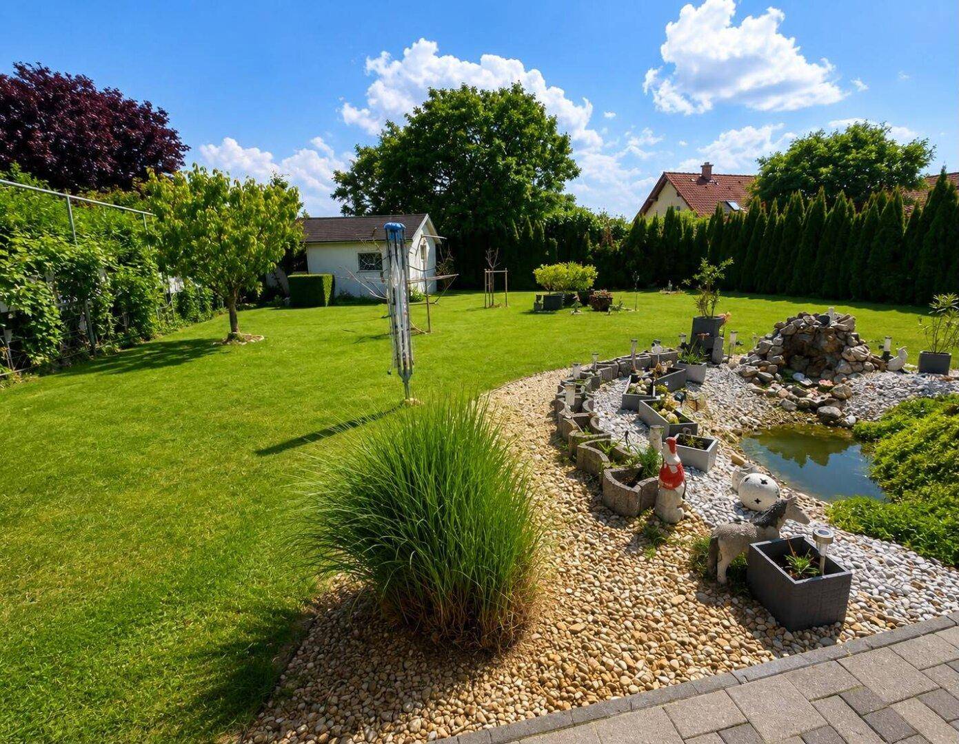 Großer, gepflegter Garten mit weitläufiger Rasenfläche, Zierpflanzen und einem kleinen Teich.
