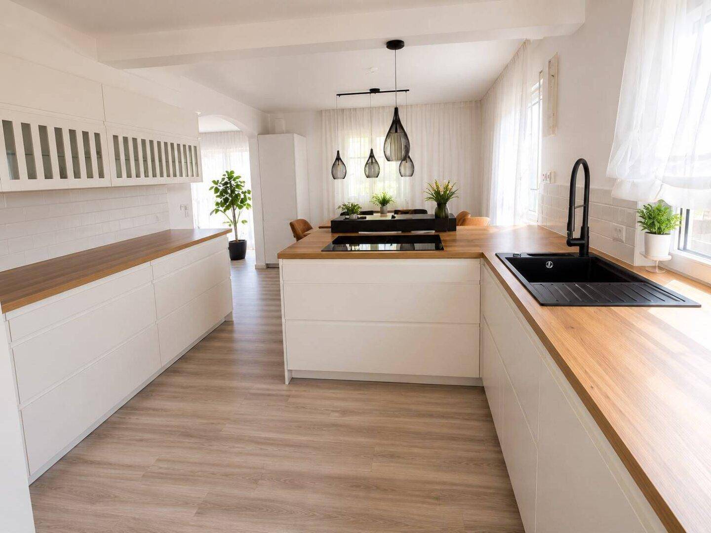Moderne weiße Küche mit Holz-Arbeitsplatten und integriertem Kochfeld, offen zum Essbereich.