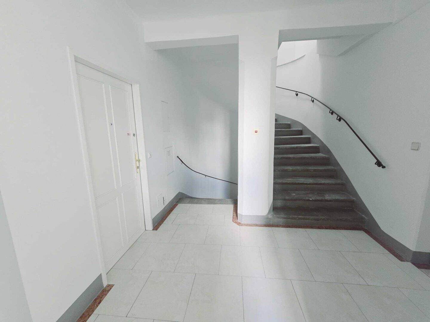 Geräumiges Treppenhaus mit geschwungener Treppe und Zugang zu den Wohneinheiten.