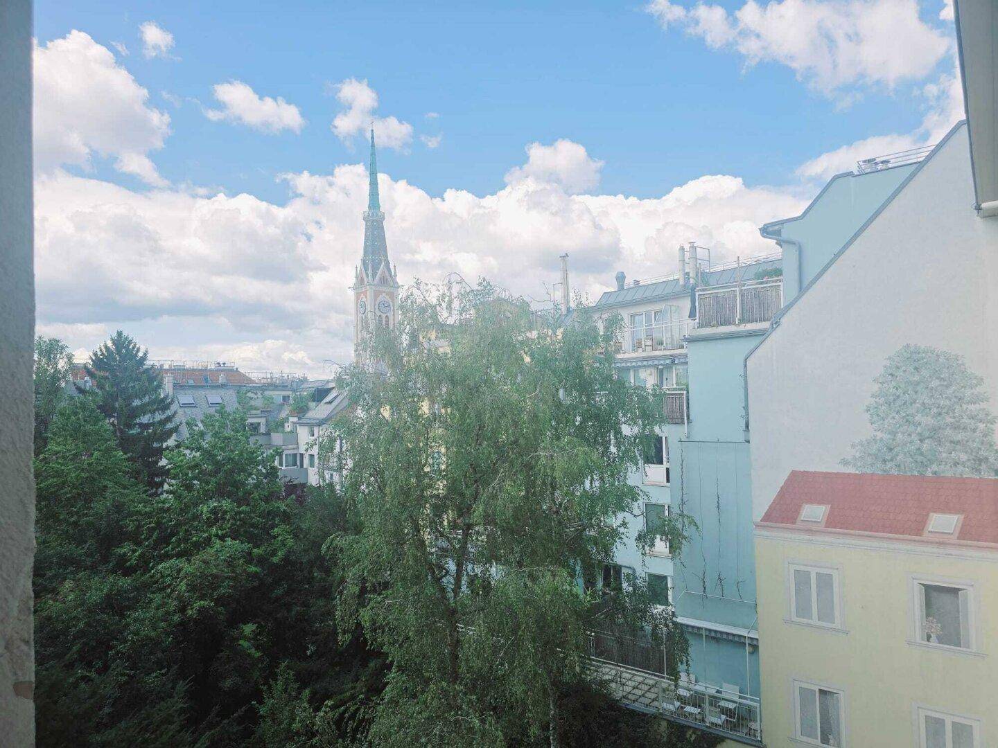 Blick aus dem Fenster auf die Stadt mit Kirchturm, Bäumen und umliegenden Gebäuden.