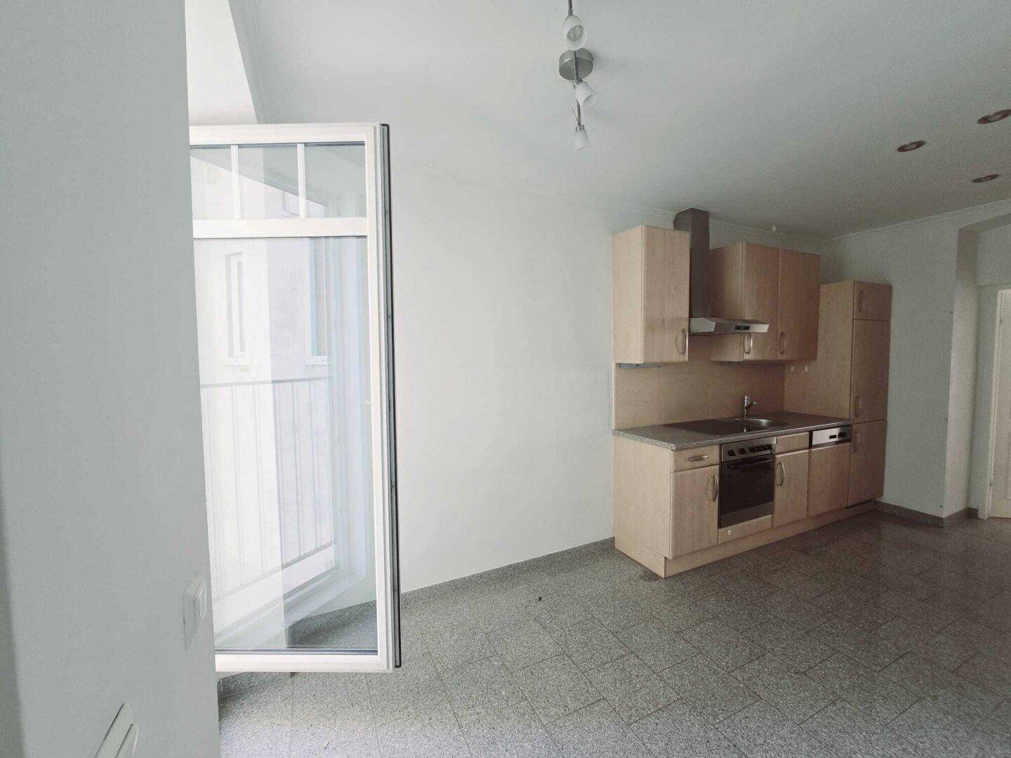 Kompakte Küche mit Holzfronten, integrierten Geräten und offenem Zugang zum Balkon.