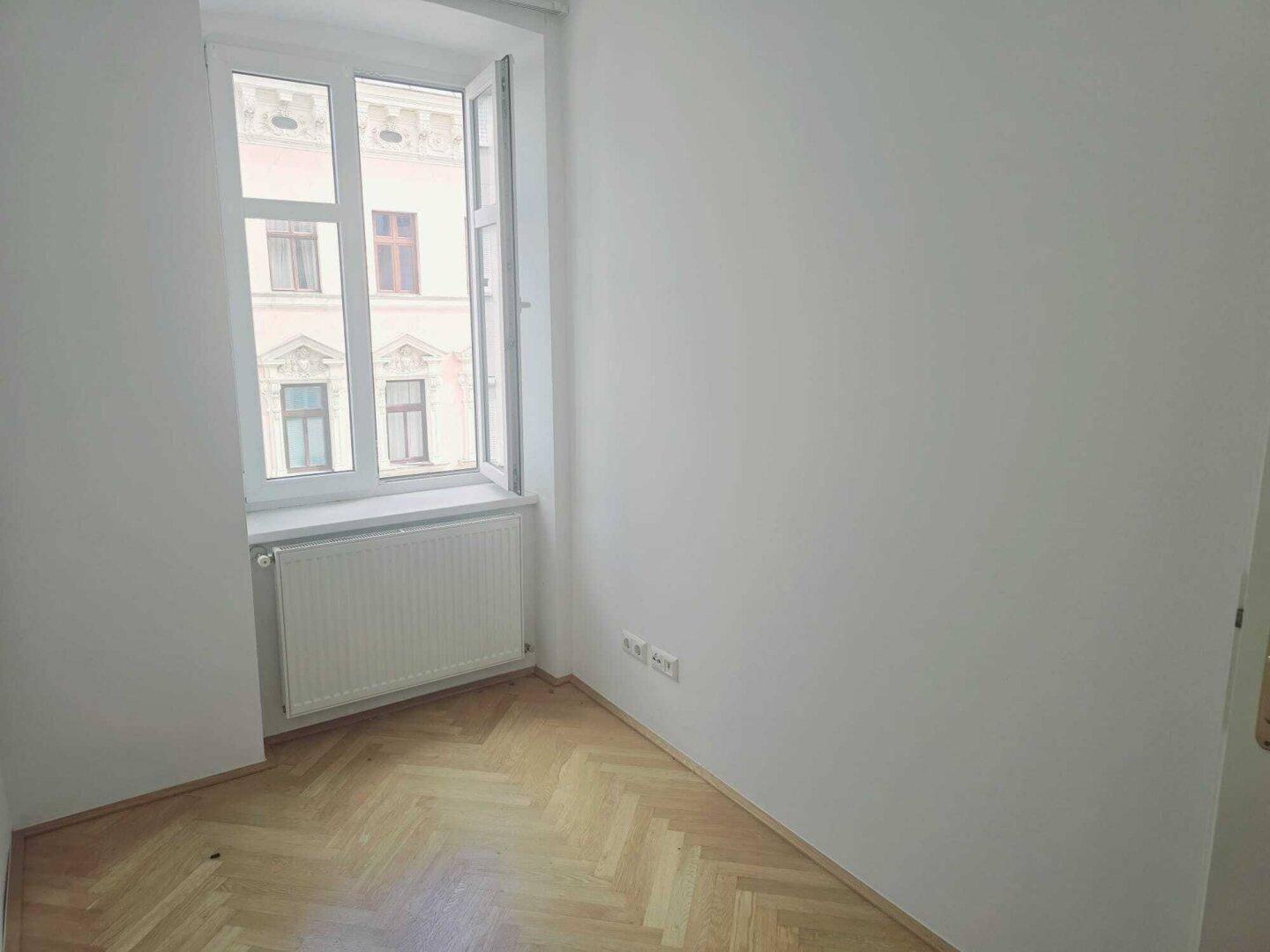 Helles Zimmer mit weiß gestrichenen Wänden und klassischem Fischgrätparkettboden.