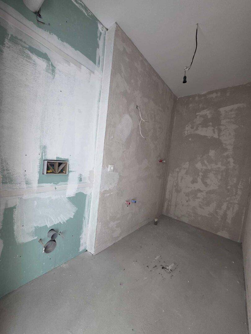 Unfertiges Badezimmer mit vorbereiteten Anschlüssen und Trockenbauwänden für den Ausbau.