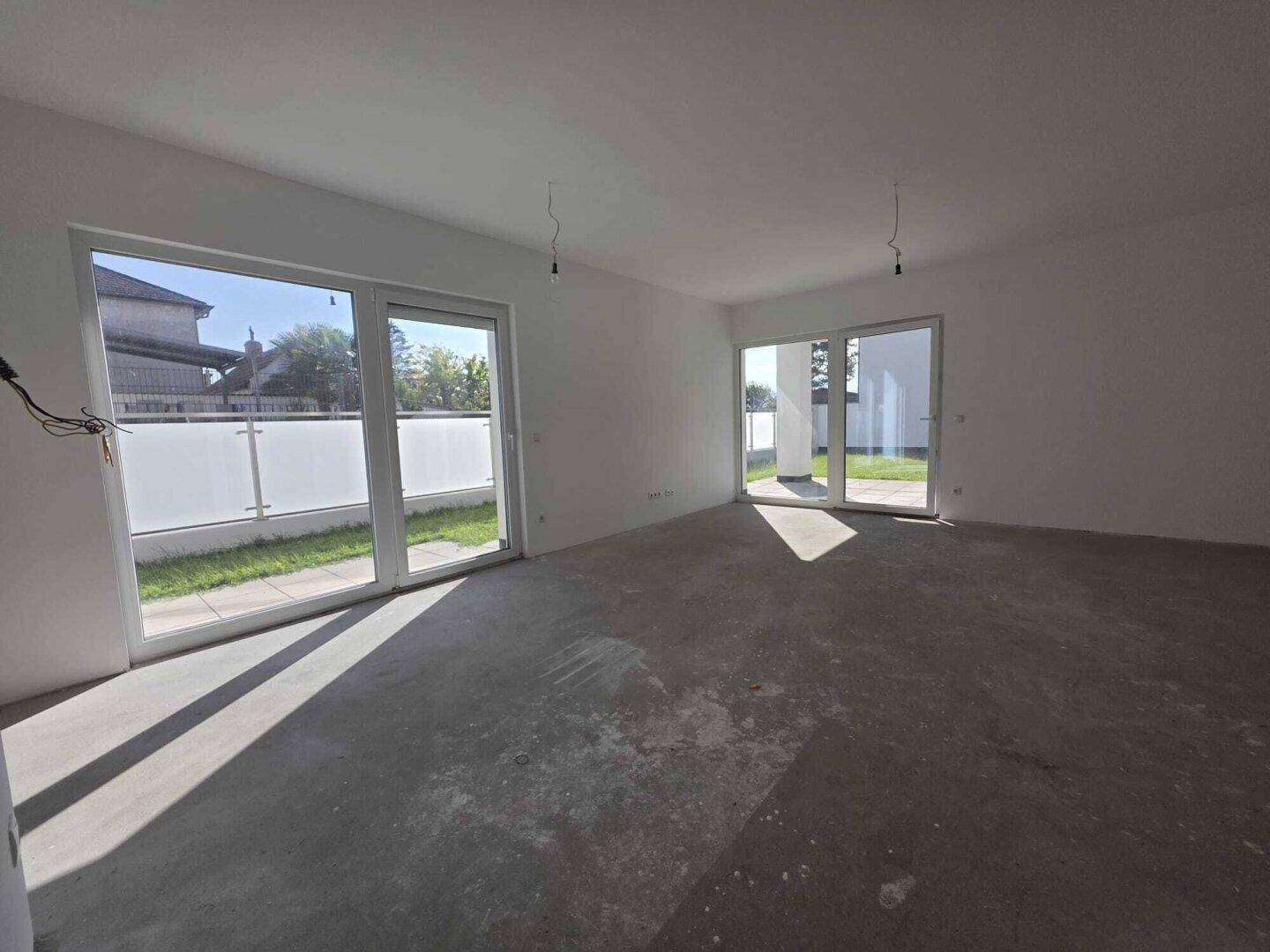 Heller, unfertiger Wohnraum mit großen Fenstern und Rohbetonboden, bereit für den Ausbau.