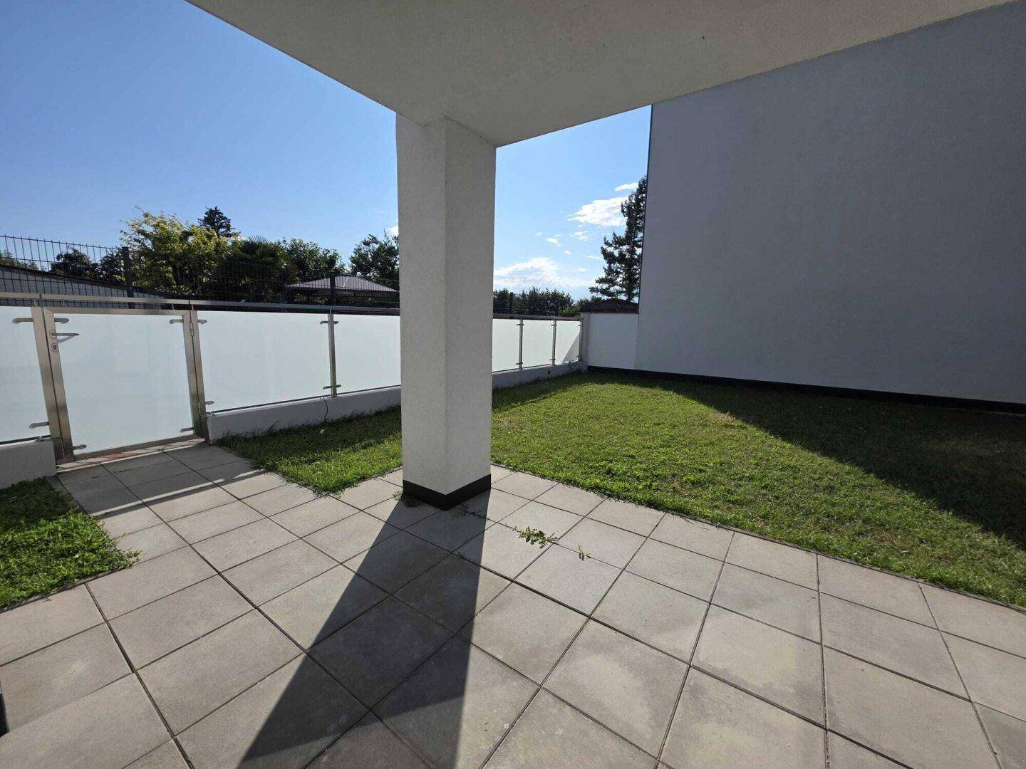 Gepflasterte Terrasse mit angrenzendem Rasenbereich und moderner Glasabtrennung.