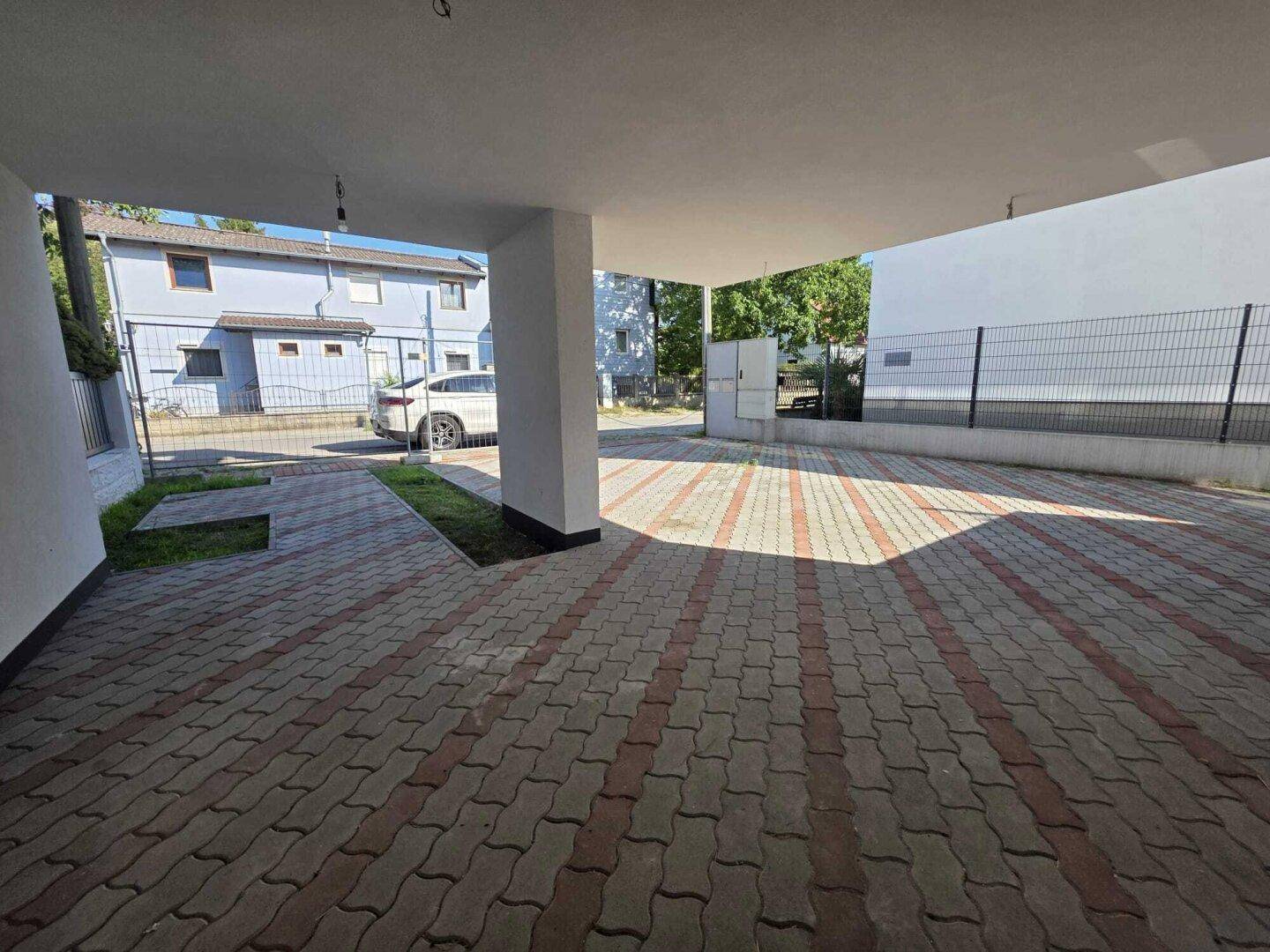 Überdachter Parkplatzbereich mit Pflastersteinen und Zugang zum Gebäude.