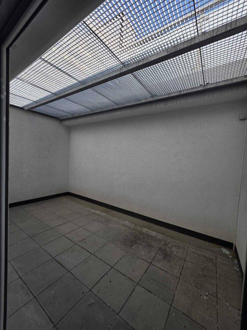 Kleiner gefliester Raum mit Gitterdach, möglicherweise als Abstellraum oder Lichtschacht genutzt.